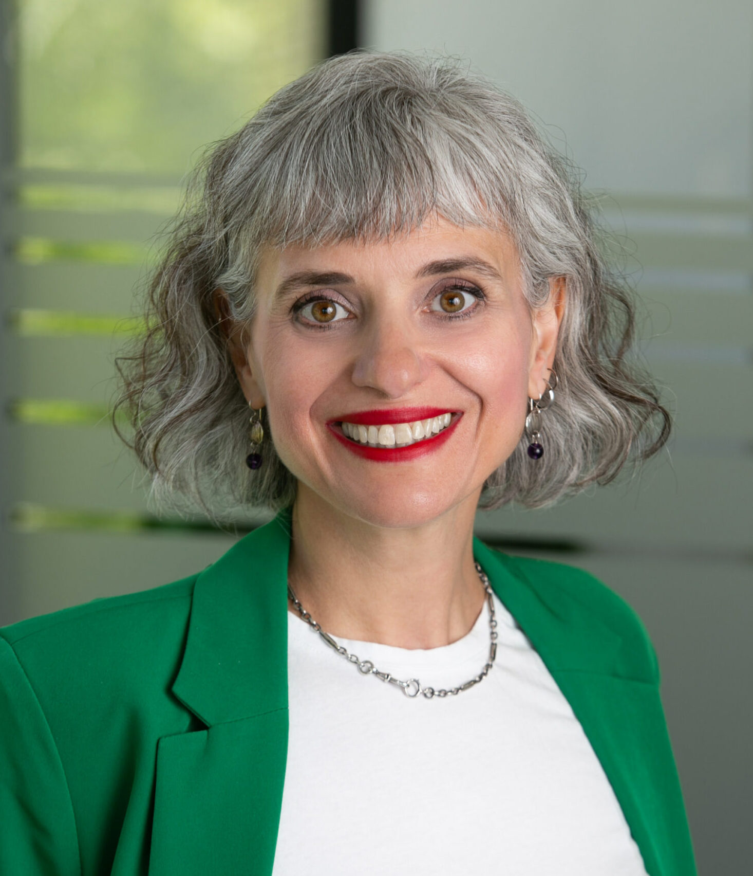 Woman with shoulder-length gray hair, wears a bright green jacket and white shirt