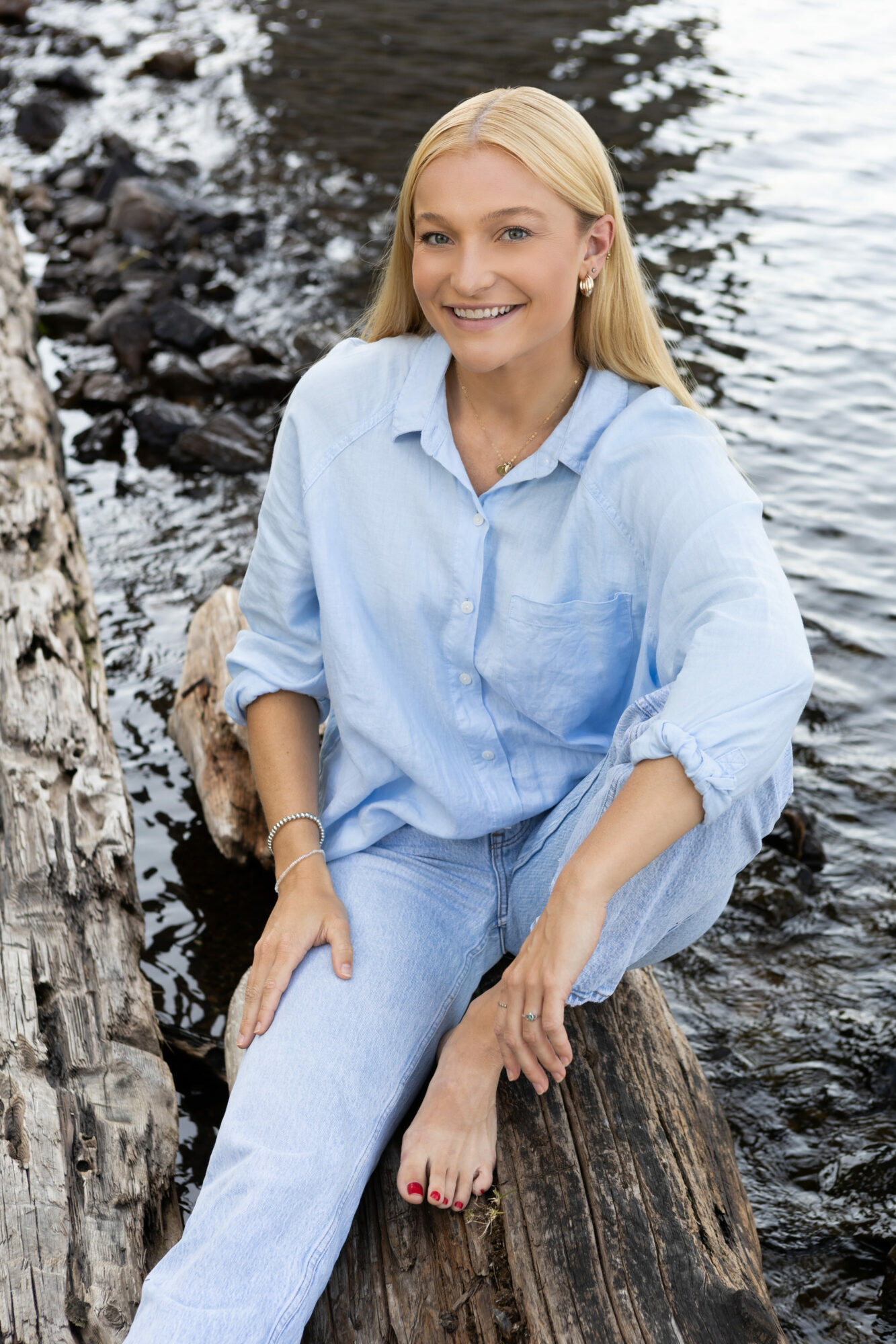 Membro do Empowered Voices vestindo camisa jeans azul claro e calça sentado à beira do lago