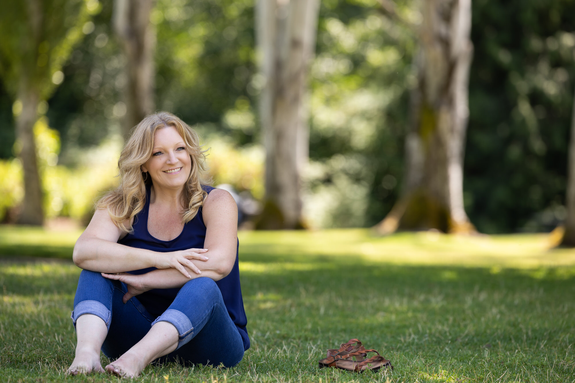 Empowered Voices member wearing black tank top and blue crop jeans on green grass and tall paperwhite tree trunks in background