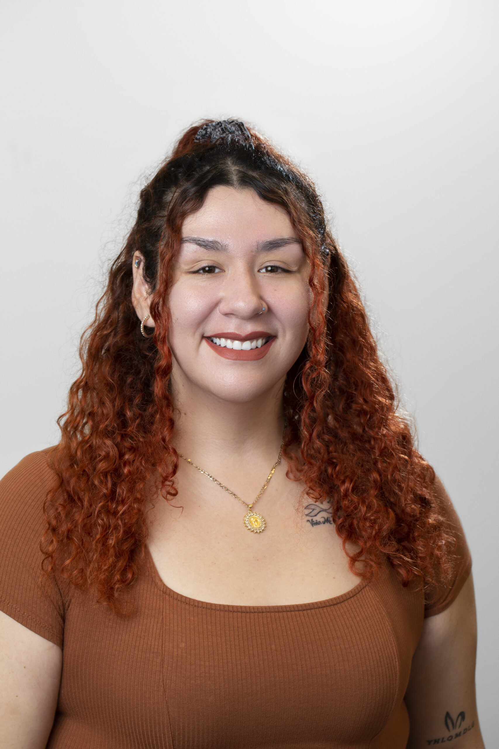 Mujer con pelo rizado rojo sonríe. Lleva un top naranja cobrizo y un collar dorado.