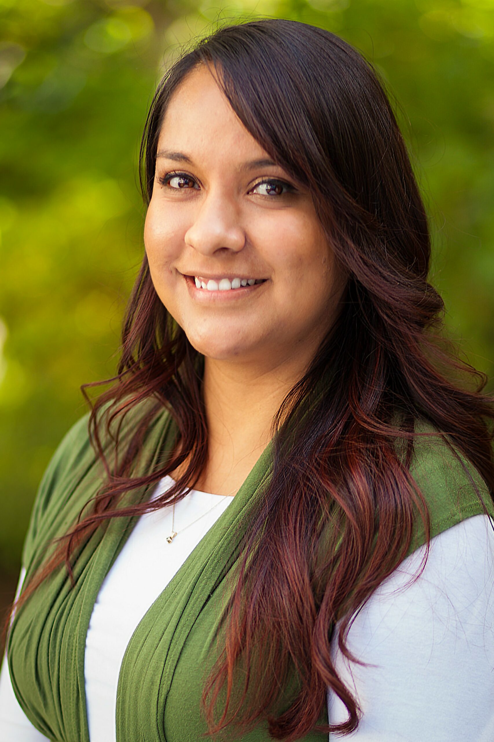 Woman with long brown hair, smiling, wearing a green vest and white shirt