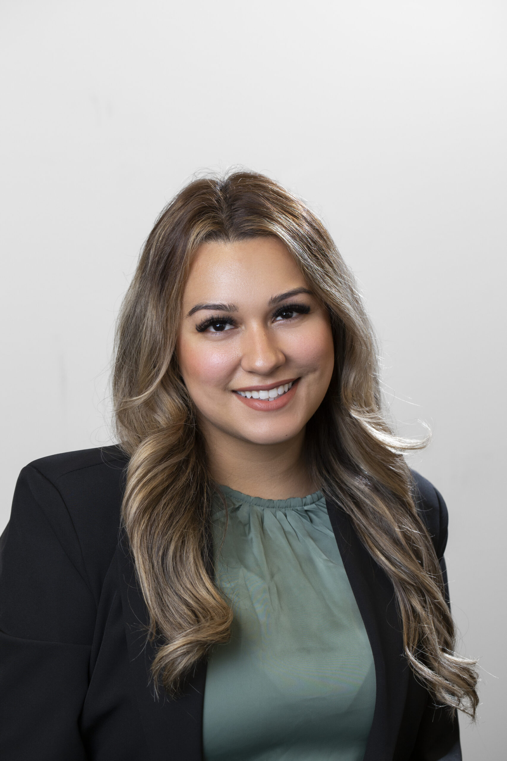 woman with long light brown hair, smiling wearing a black blazer and green blouse.