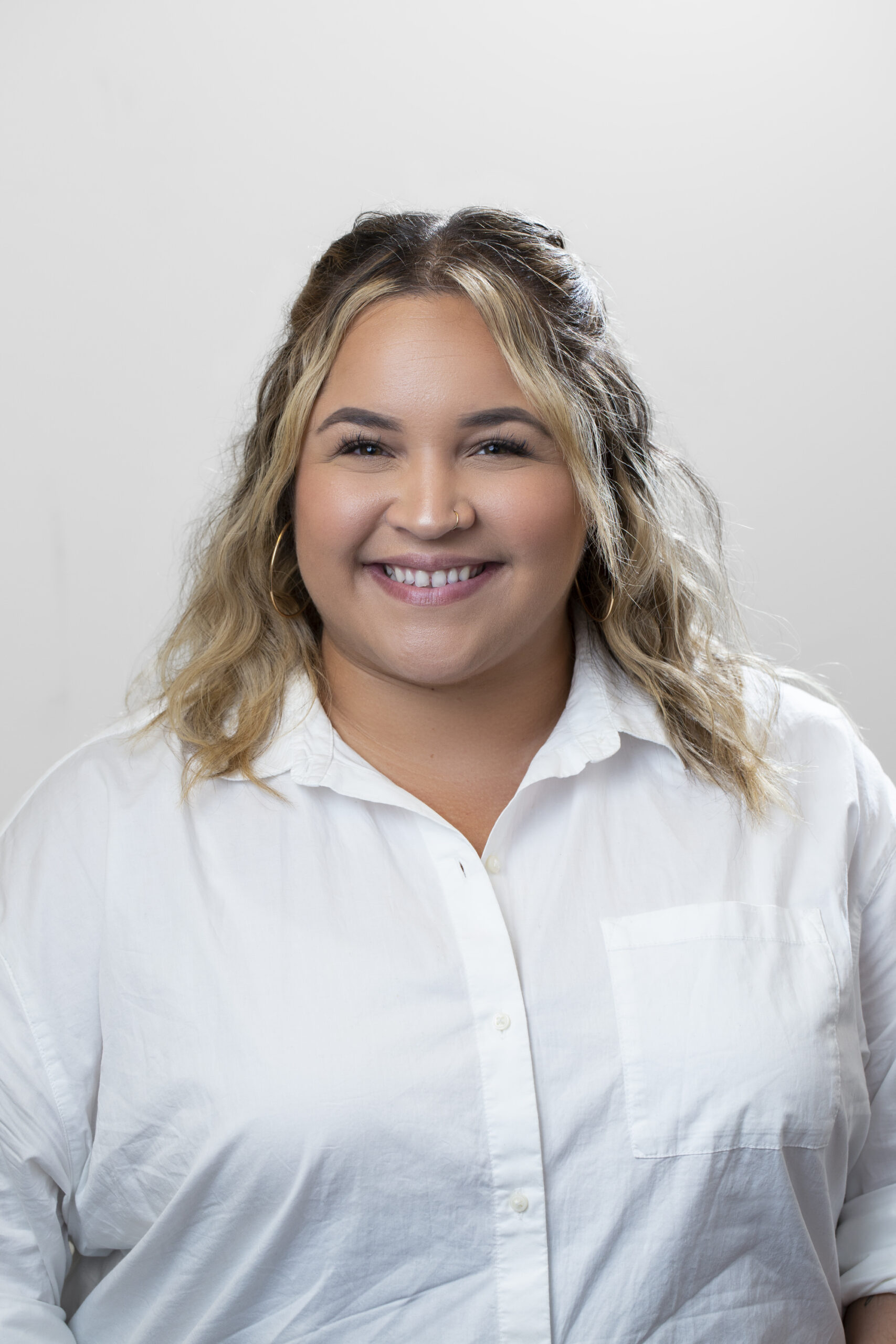 mulher sorridente, com cabelo castanho claro na altura dos ombros, vestindo uma blusa branca.