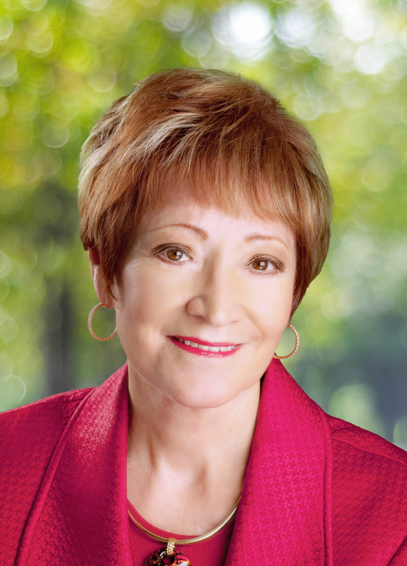 Woman with short auburn hair smiling, wearing a fuchsia blazer and blouse.
