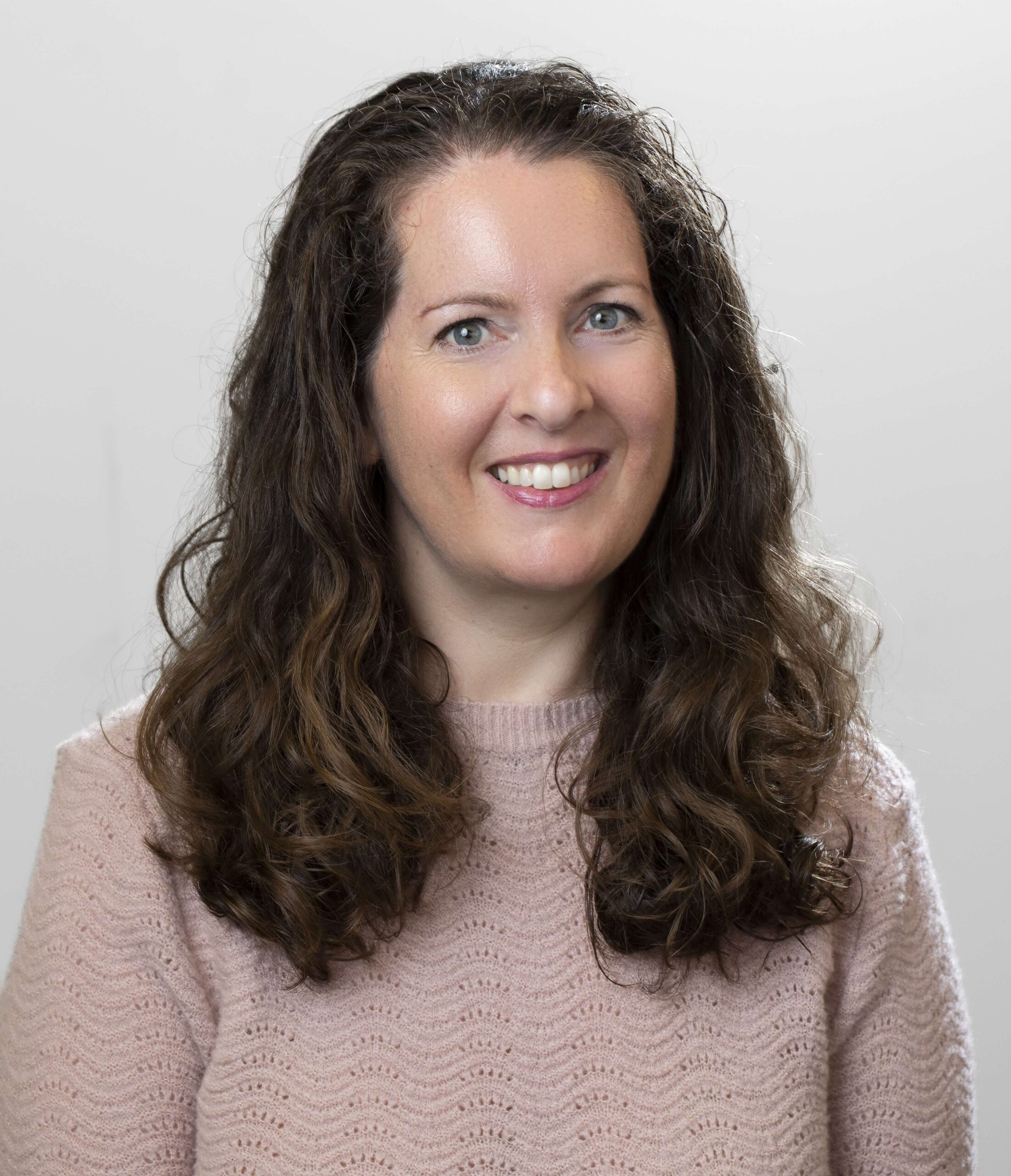 smiling woman with long brown hair wearing pink sweater
