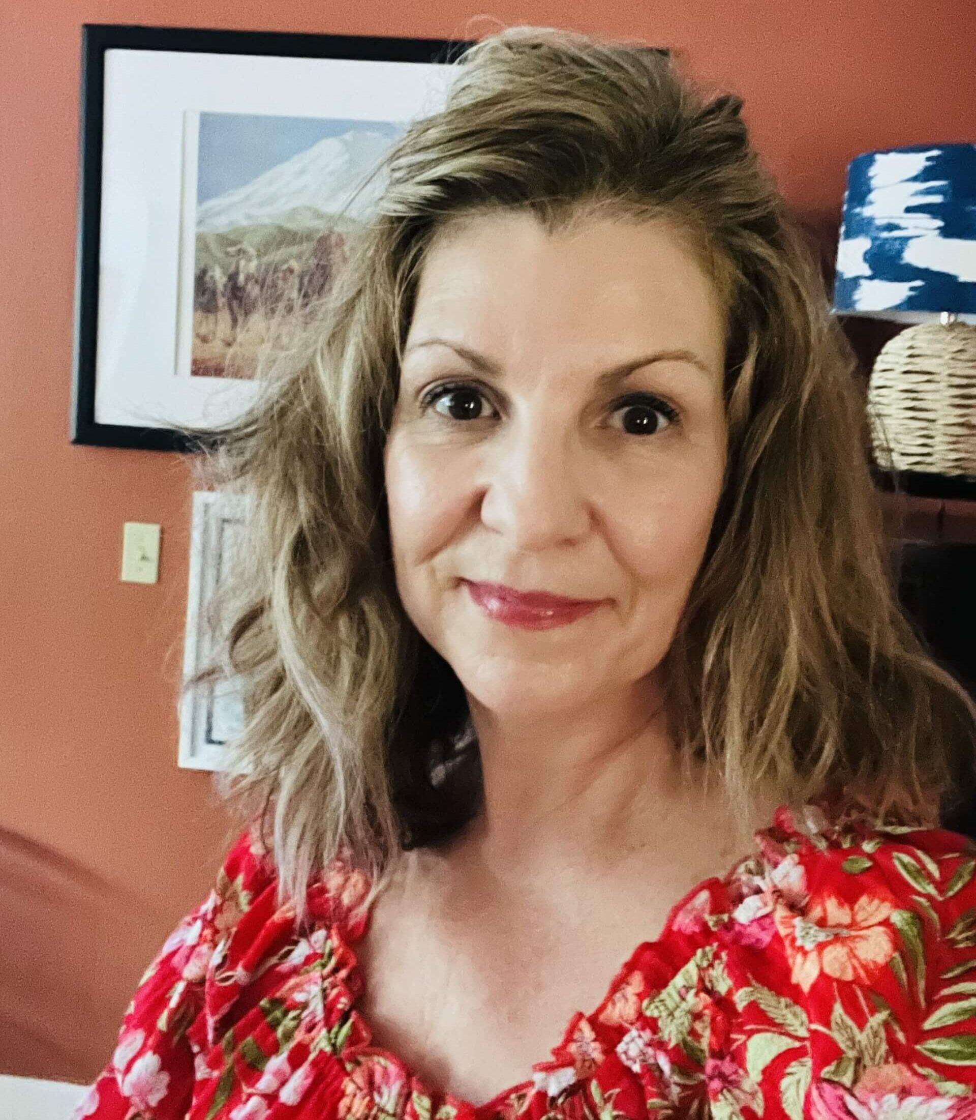 woman with medium brown hair, wearing a red floral print top