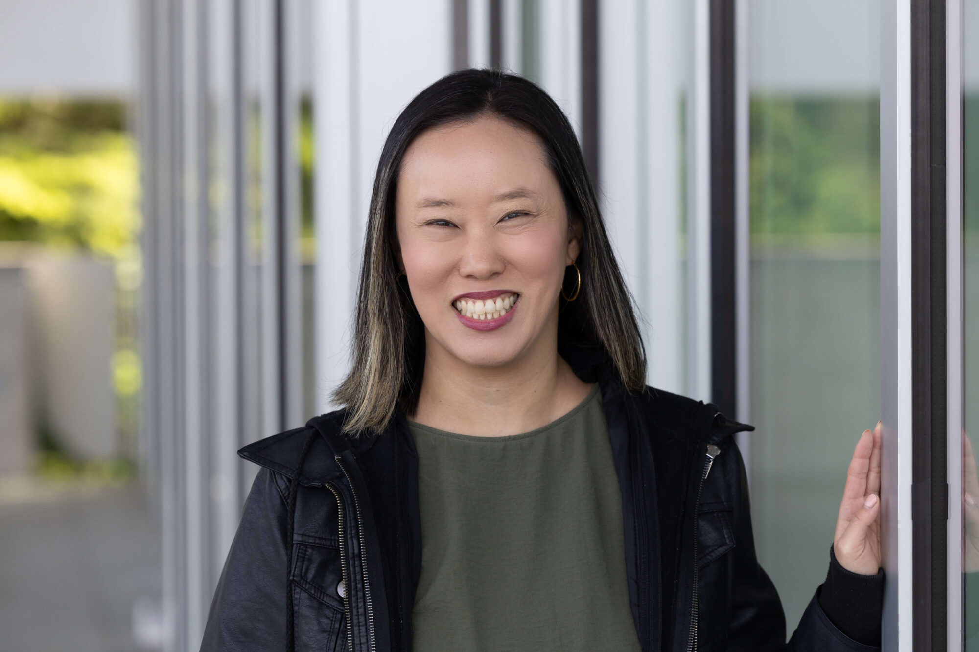 Woman smiling, with medium brown hair, olive green shirt and black jacket