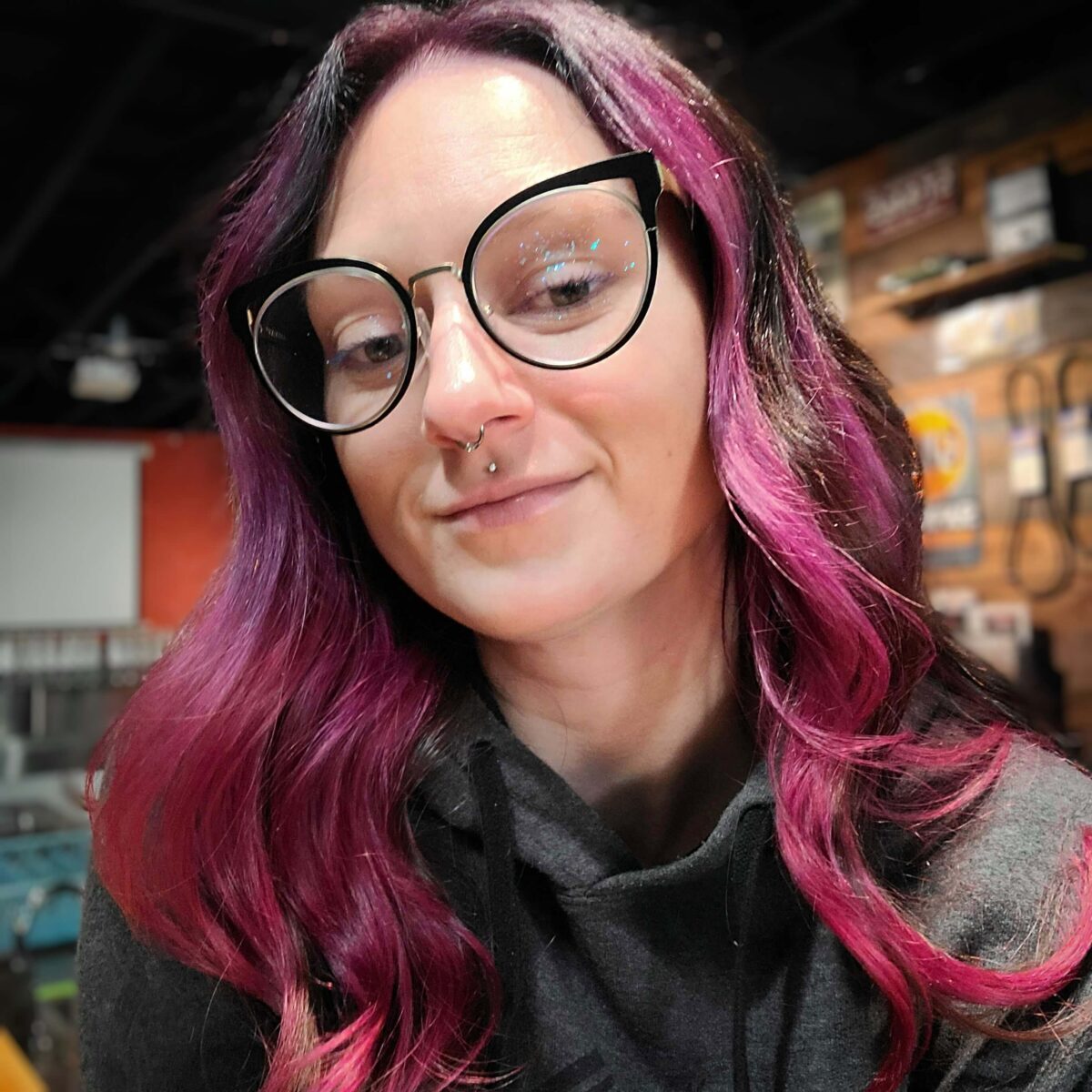Frau mit kleinem Lächeln, langen rosa und braunen Haaren und schwarzer Brille