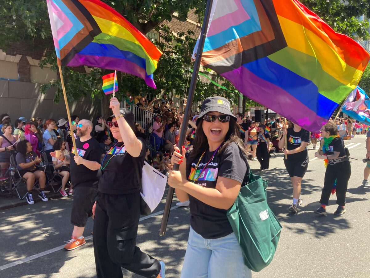 KCSARC staff march with GSBA staff in the Seattle Pride Parade, smiling and waving Pride flags.