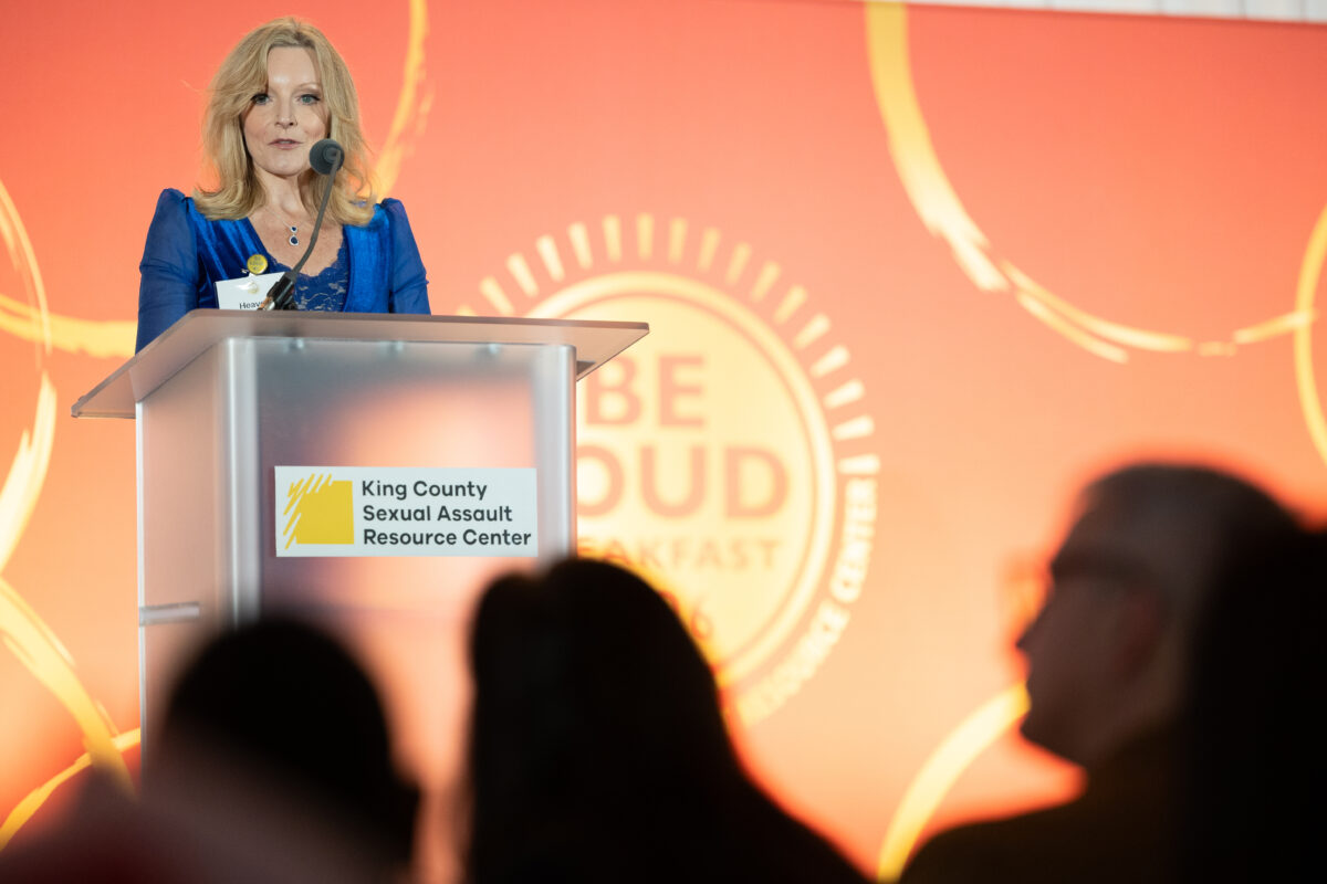 A client speaker shares her story from the podium during the 2026 BE LOUD Breakfast event.