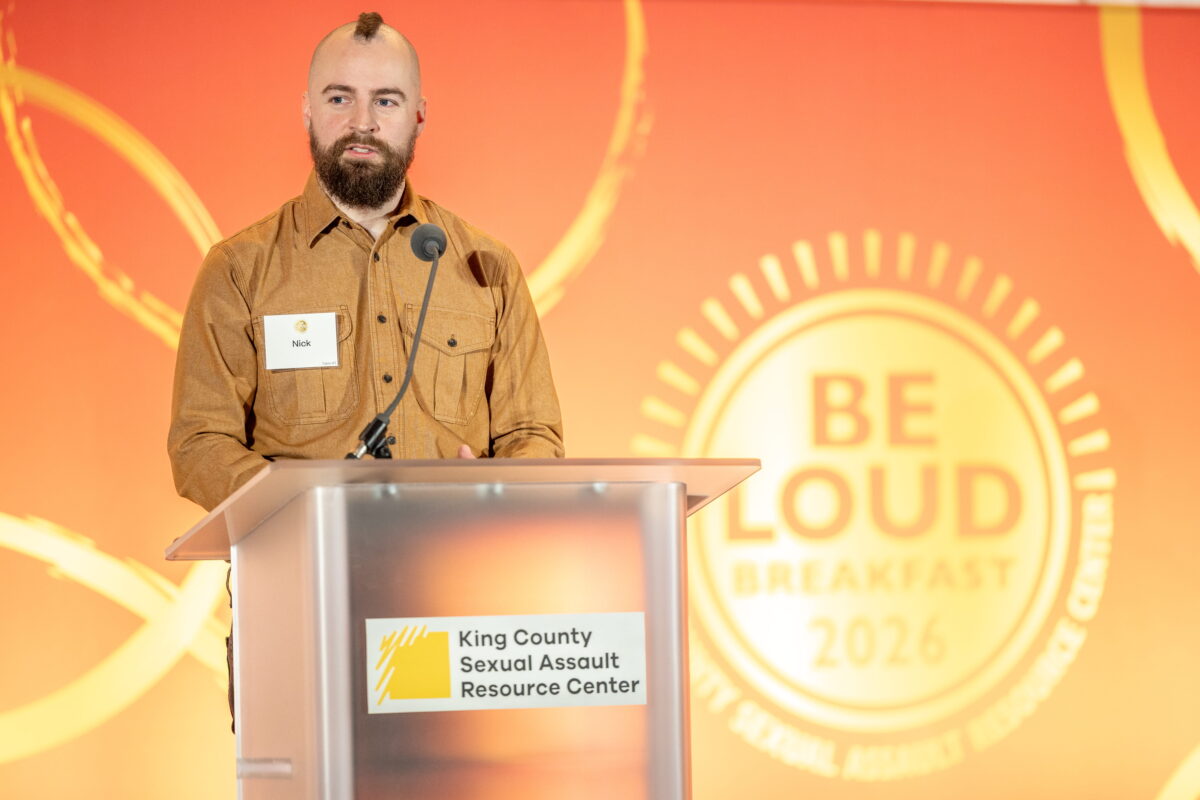 A client speaker shares his story from the podium during the 2026 BE LOUD Breakfast event.
